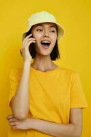 young woman yellow t-shirt and Hat summer style with phone yellow background photo