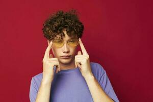 retrato de un joven Rizado hombre en amarillo lentes púrpura camiseta emociones estilo de vida foto