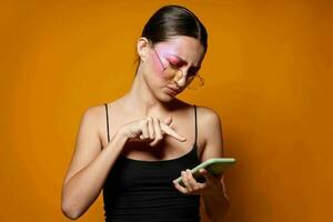 Sexy brunette woman with phone pink face makeup posing attractive look glasses yellow background unaltered photo