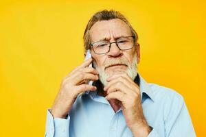 Photo of retired old man talking on the phone posing close-up yellow background