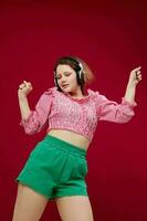 energetic young girl in green shorts listening to music Red background unaltered photo