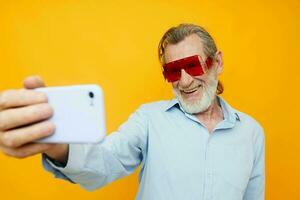 alegre mayor hombre en de moda lentes con teléfono amarillo antecedentes foto