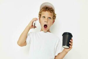linda chico en un blanco camiseta gorra con un teléfono en un vaso con un bebida aislado antecedentes inalterado foto