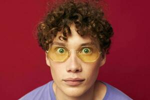 retrato de un joven Rizado hombre en amarillo lentes púrpura camiseta emociones estilo de vida foto