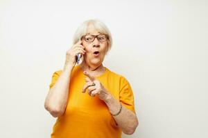 elderly woman in a yellow t-shirt posing communication by phone light background photo