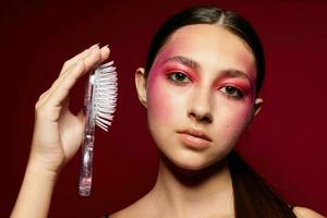 Young beautiful woman with a comb in hand bright makeup posing fashion emotions pink background unaltered photo