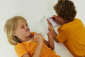 imagen de positivo chico y niña dibujo en cuadernos acostado en el piso ligero antecedentes inalterado foto