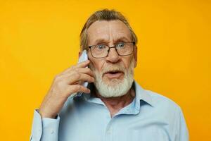 Photo of retired old man talking on the phone posing close-up yellow background