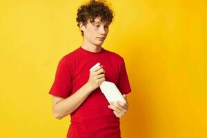 Young curly-haired man in a red t-shirt detergents in hands posing Lifestyle unaltered photo