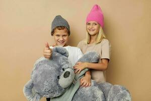 Photo of two children in multi-colored hats entertainment posing beige background