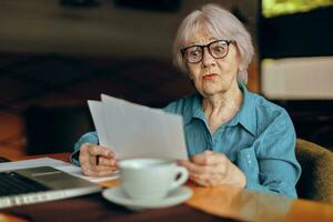 retrato de un mayor mujer sentado en un café con un taza de café y un ordenador portátil persona de libre dedicación trabajos inalterado foto