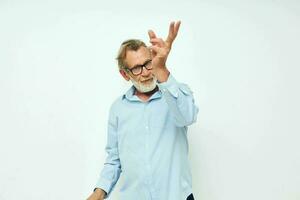 retrato de contento mayor hombre en azul camisas gestos con su manos ligero antecedentes foto