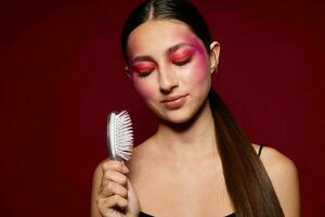 Young beautiful woman with a comb in hand bright makeup posing fashion emotions pink background unaltered photo