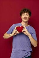 red-haired curly guy a box in the form of a heart in his hands red background photo