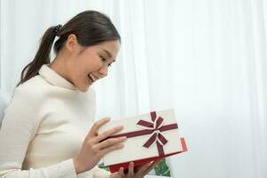 una mujer bastante asiática se siente sorprendida y mira interesada dentro de la caja de regalos. linda chica emocionada caja de regalo abierta. cumpleaños, celebración, navidad, festival de año nuevo, gracias, celebrar, día de san valentín, aniversario foto