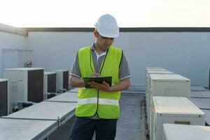 asiático mantenimiento ingeniero trabajos en el techo de fábrica. contratista inspeccionar compresor sistema y planes instalación de aire condición sistemas en construcción. Lista de Verificación, inspector, controlar foto