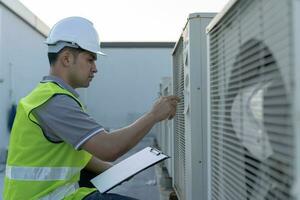 asiático mantenimiento ingeniero trabajos en el techo de fábrica. contratista inspeccionar compresor sistema y planes instalación de aire condición sistemas en construcción. Lista de Verificación, inspector, controlar foto