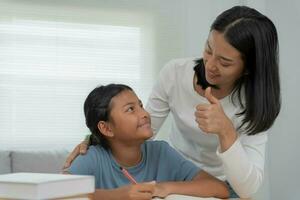 Mother teaching lesson for daughter. Asian young little girl learn at home. Do homework with kind mother help, encourage for exam.. Girl happy Homeschool. Mom advice education together. photo