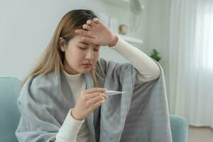 Young Asian woman having high fever while checking body temperature, female sneezing and runny nose with seasonal influenza, allergic, digital thermometer, virus, coronavirus, illness, respiratory photo