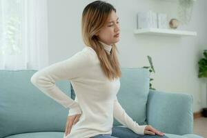 Asia beautiful woman holding her lower back while and suffer from unbearable pain health and problems, chronic back pain, backache in office syndrome, scoliosis, herniated disc, muscle inflammation photo