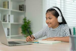 online tutor online course for Asian children. video conference on laptop at home. play back online course, girl student wear earphones to study, notes homework, video classes, new education. photo