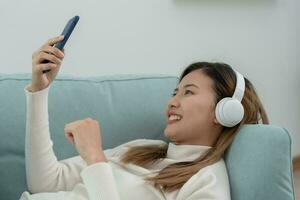 Joyful young Asian women in wireless headphones sitting and enjoy music, having fun, listening to music, raising his arm, dancing to favorite song, enjoying cool soundtrack, happy life, recreation photo