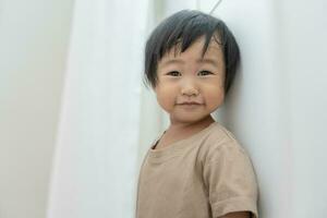 little asian children kid girl covering his eyes with hands, playing hide and seek standing next a wall house, Adorable child having fun in the home. happy family have fun with kids, activity photo