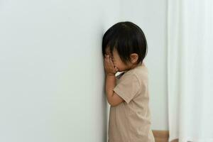 little asian children kid girl covering his eyes with hands, playing hide and seek standing next a wall house, Adorable child having fun in the home. happy family have fun with kids, activity photo