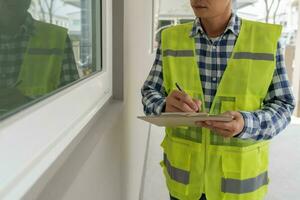 el inspector o ingeniero está inspeccionando la construcción y el aseguramiento de la calidad de la nueva casa usando una lista de verificación. ingenieros o arquitectos o contratistas trabajan para construir la casa antes de entregársela al propietario foto