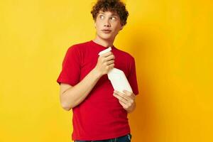 cute red-haired guy in a red t-shirt detergents in hands posing yellow background unaltered photo