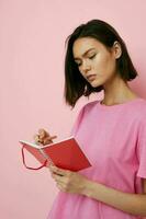 joven hermosa mujer en un rosado camiseta rojo cuaderno y bolígrafo rosado antecedentes foto