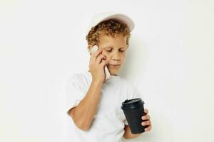 linda chico en un blanco camiseta gorra con un teléfono en un vaso con un bebida estilo de vida inalterado foto