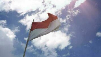 The red and white Indonesian flag flutters in the wind, with a background of sky clouds and sunlight video