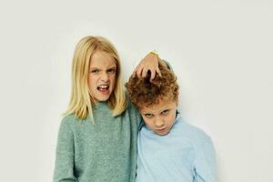 Photo of two children in multi-colored sweaters posing for fun light background