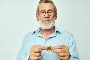 Senior grey-haired man finance gold coins bitcoin posing light background photo