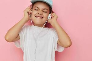 little girl headphones in a white t-shirt and a cap pink background photo