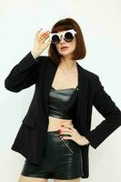 attractive woman posing with sunglasses a leather suit black jacket light background photo
