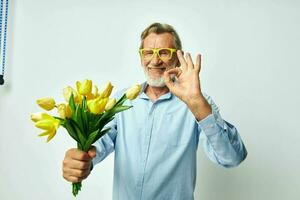 Photo of retired old man in a blue shirt with a bouquet of flowers light background