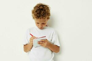 a boy in a white t-shirt draws with a pencil in a notebook photo