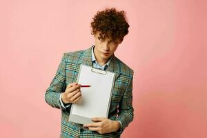 cute red-haired guy folder for papers blank sheet posing in suit pink background unaltered photo