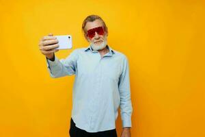 old man in fashionable red glasses with a phone yellow background photo