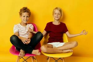 two joyful children childhood sitting on chairs together on colored background photo