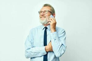 old man in glasses with a phone in the studio on a white background talking photo