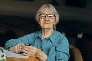 Happy senior woman with glasses sits at a table in front of a laptop Retired woman chatting unaltered photo