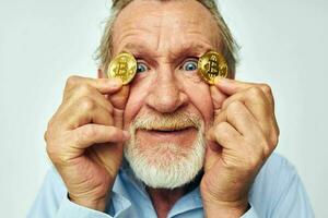 Senior grey-haired man finance gold coins bitcoin near face light background photo