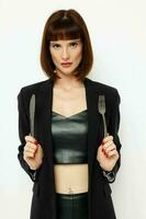 beautiful woman in a black jacket a knife and a fork near the face light background photo