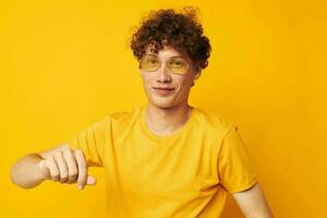 Young curly-haired man yellow t-shirt glasses fashion hand gestures monochrome shot photo