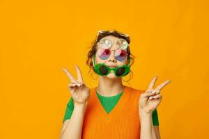 portrait of a young woman multicolored sunglasses on face posing grimace yellow background unaltered photo