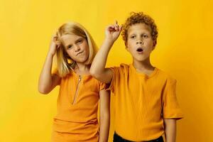 Boy and girl in yellow t-shirts standing side by side childhood emotions yellow background photo