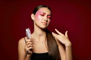 bonito mujer rosado cara maquillaje posando atractivo Mira con un peine de cerca inalterado foto